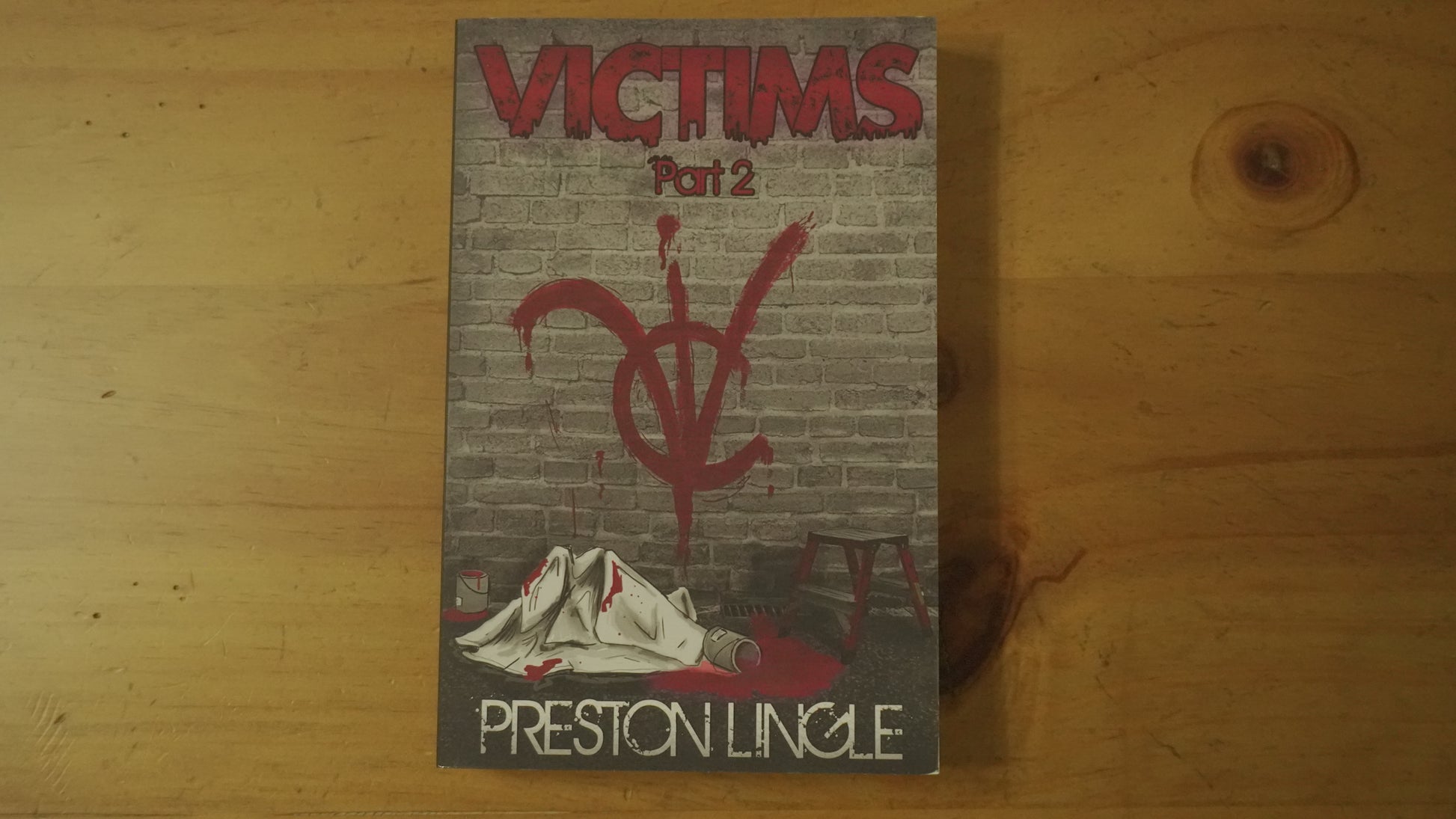 Front cover of the paperback version of the book titled 'Victims Part 2' by Preston Lingle on a wooden surface