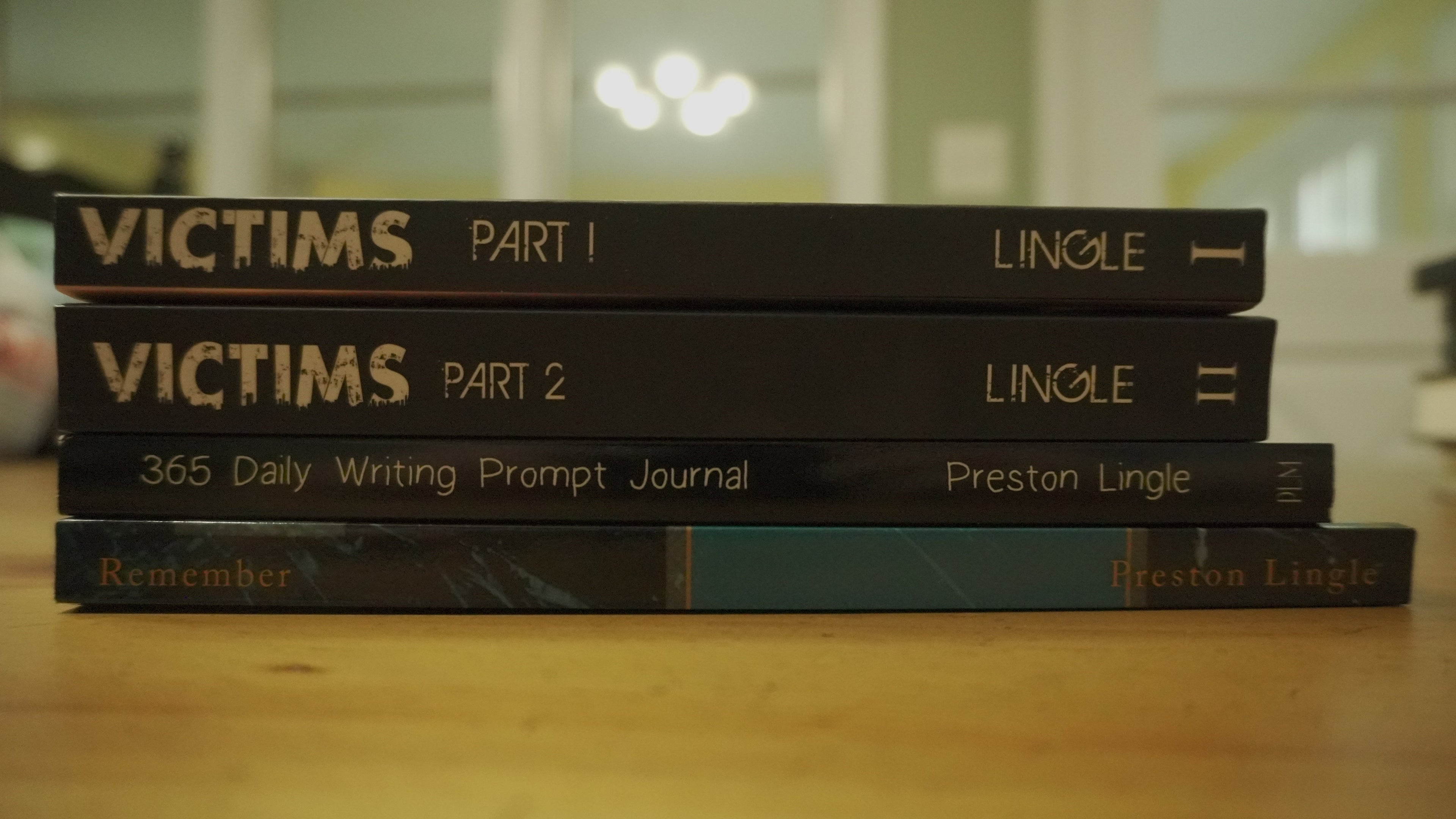 Stack of books titled 'Victims Part 1', 'Victims Part 2', and '365 Daily Writing Prompt Journal' by Preston Lingle on a wooden surface.